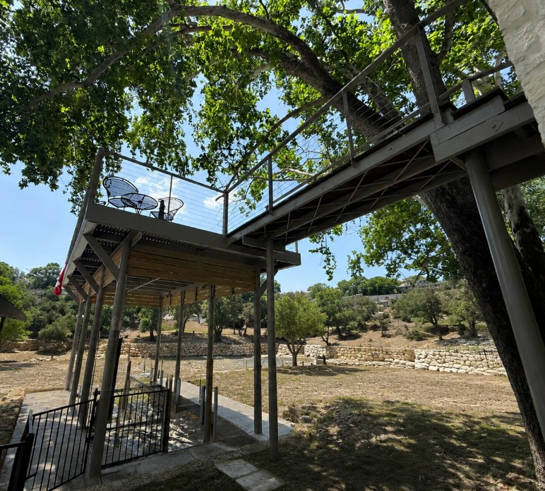 Elevated concrete deck on steel pipe pilings with cable rail and covered pergola below, Texas Hill Country — built by Wulfhe Outdoor Living